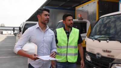 Two men, one holding a hard hat and clipboard, standing near trucks at a logistics yard