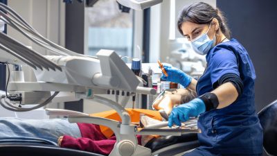 Dentist wearing a mask and gloves treating a patient in a dental chair