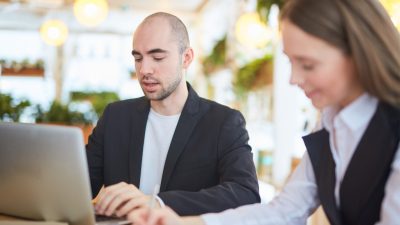 Two coworkers reviewing documents together at a laptop in an office